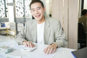 asian man in suit sitting at desk with calculator photo