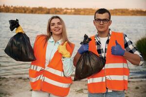 Showing, fingers up, smiling, finished..A volunteers collects garbage on a muddy beach photo