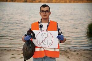 Text 'no plastic', on poster. Man volunteer is against Earth pollution by trash, outdoors photo
