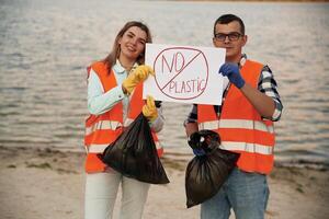 Poster ,with 'no plastic' text.. A volunteers collects garbage on a muddy beach photo
