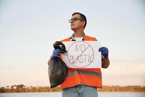 Text,, 'no plastic',, on poster. Man ,volunteer is against Earth pollution by trash, outdoors photo