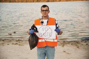 Text, 'no plastic' on poster. Man volunteer is against Earth pollution by trash, outdoors photo