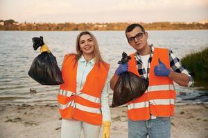 Showing fingers up, smiling,, finished. A volunteers collects garbage on a muddy beach photo