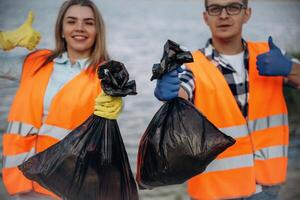 Showing ,fingers up, smiling, finished. A volunteers collects garbage on a muddy beach photo