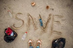 Top, view of sand with word save, trash on the ground, legs of the person, conception of ecology photo