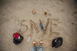 Top view, of sand with word save, trash on the ground, legs of the person, conception of ecology photo
