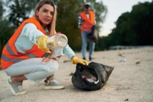 Picking ,up the .bottle. A volunteers collects garbage on a muddy beach photo