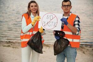 Poster ,with 'no plastic' text. A volunteers collects garbage on a muddy beach photo