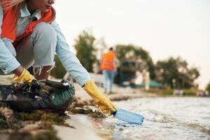 Picking bottle, from the water. A volunteers collects garbage on a muddy beach photo