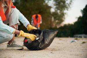 Picking up, the bottle. A volunteers collects garbage on a muddy beach photo