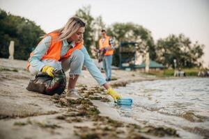 Picking, bottle from the water. A volunteers collects garbage on a muddy beach photo
