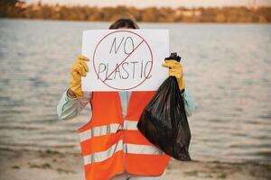 Text,, 'no plastic' on poster. Man,, volunteer is against Earth pollution by trash, outdoors photo