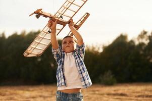 Boy ,is,, playing ,with ,,wooden toy plane outdoors on the field photo