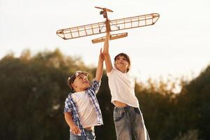 Boy and girl are playing with wooden toy plane on the field,, photo