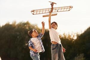 Boy and, girl ,are,, playing with wooden toy plane on the field photo