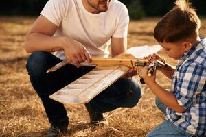 Messing ,around with,, broken toy. Father and son are with wooden plane on the field photo