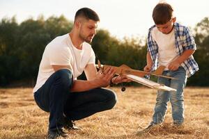 Focused ,by ,fixing ,the toy. Father and son are with wooden plane on the field photo