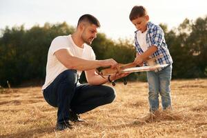 Focused ,by ,fixing,, the toy. Father and son are with wooden plane on the field photo