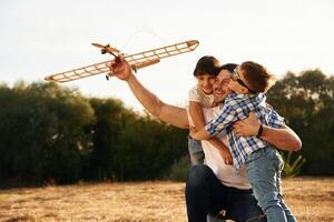 Sitting, side, view.... Family of father, son and daughter are playing with wooden toy plane on the field photo