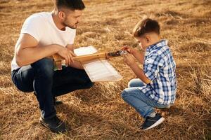 Focused ,by,, fixing the toy. Father and son are with wooden plane on the field photo
