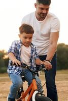 Teaching how to ride., Dad with son are with bicycle on the field outdoors photo
