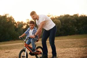Teaching, how to ride. Dad ,with son are with bicycle on the field outdoors photo