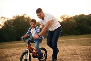 Teaching how to ride. Dad ,,with son are with bicycle on the field outdoors photo