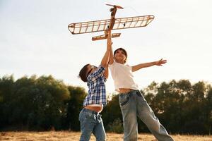 Flying high up. Boy and,, girl ,are playing with wooden toy plane on the field photo