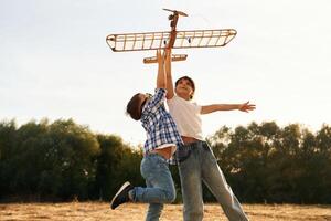 Flying high, up. Boy ,and girl are playing with wooden toy plane on the field photo
