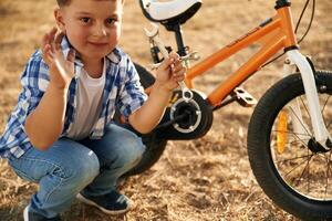 Holding wrench. Cute boy, is ,with his bicycle on the field photo