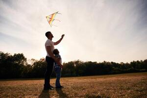 Father, and son are ,with kite on the field, illuminated by sunlight photo