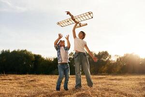 Having fun. .Boy and girl are playing with wooden toy plane on the field photo