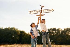 Flying ,high up. Boy and girl are playing with wooden toy plane on the field photo