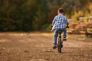 Riding,, having fun. Cute boy is with his bicycle on the field photo