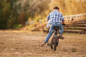 Riding, having, fun. Cute boy is with his bicycle on the field photo