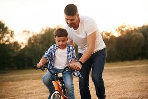 Teaching, how, to ride. Dad with son are with bicycle on the field outdoors photo