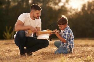 Handmade toy plane is broken, fixing it. Father and son are on the field photo