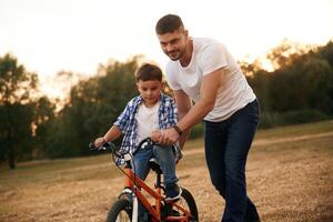 Teaching, how to ride. Dad with son are with bicycle on the field outdoors photo