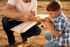 Messing, around with broken toy. Father and son are with wooden plane on the field photo