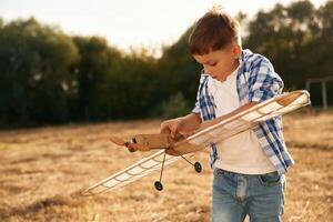 Fixing, the ,toy. Boy is playing with wooden plane outdoors on the field photo