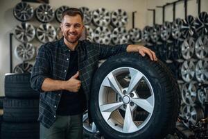 Smiling,, positive facial, expression,,, hand gesture. Man worker is maintenance station with tires, wheels photo
