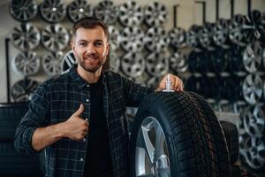 Smiling, positive facia,,,,l expression, hand gesture. Man worker is maintenance station with tires, wheels photo