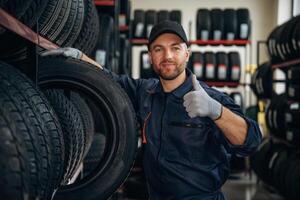Friendly, facial ,,,,expression, in cap. Man worker is maintenance station with tires, wheels photo