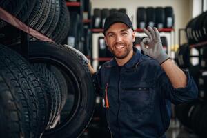Friendly facial expression,, in, cap.. Man worker is maintenance station with tires, wheels photo