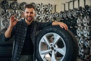 Smiling,, positive ,facial ,,expression, hand gesture. Man worker is maintenance station with tires, wheels photo