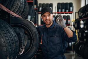 Friendly facial expression, in cap. ..Man worker is maintenance station with tires, wheels photo