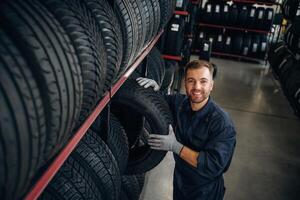 In ,professional uniform near the shelve... Man worker is maintenance station with tires, wheels photo