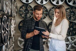 Male worker with ,woman in the car maintenance room, holding digital tablet, reading it photo