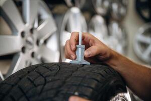 Tool in hand,,,, checking the quality. Man worker is maintenance station with tires, wheels photo