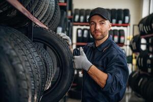 Friendly,, facial, expression, in cap. Man worker is maintenance station with tires, wheels photo